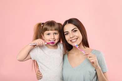 Little girl and her mother brushing teeth together on color background
