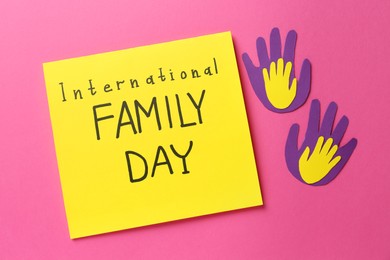 Paper palms and card with text International Family Day on pink background, flat lay