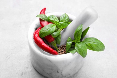 Photo of Mortar with peppercorns, basil and chilli pepper on light grey table, closeup