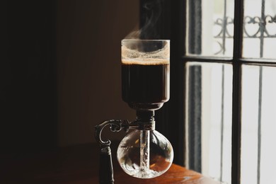 Photo of Vacuum coffee maker on wooden table in cafe