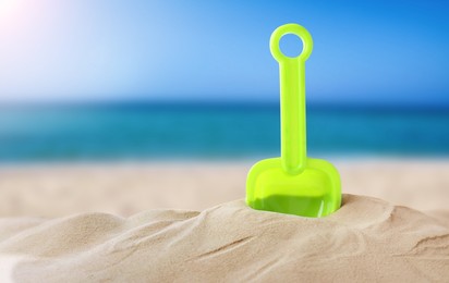 Green plastic toy shovel sandy beach near sea, space for text 