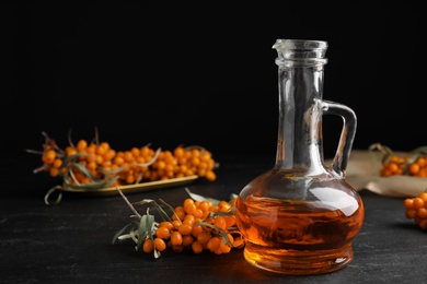 Ripe sea buckthorn and jug of essential oil on black table. Space for text