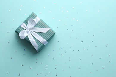 Gift box and confetti stars on light blue background, flat lay. Christmas celebration