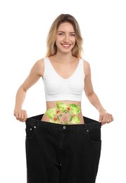 Slim young woman wearing oversized jeans and images of vegetables on her belly against white background. Healthy eating