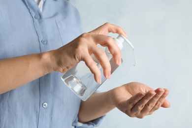 Woman applying antiseptic gel onto hand against light background, closeup. Virus prevention