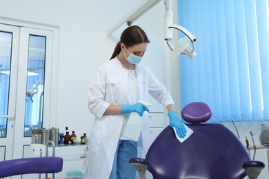Professional dentist in white coat and medical mask cleaning workplace with antiseptic indoors