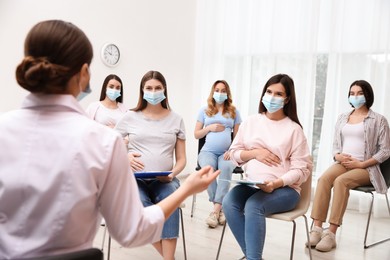 Group of pregnant women in protective masks with doctor at courses for expectant mothers indoors