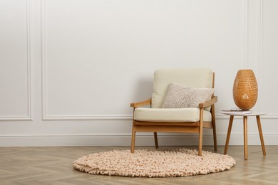 Stylish armchair with cushion and lamp near white wall indoors, space for text. Interior design