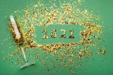 Flat lay composition with confetti and champagne glass on green background. New Year celebration