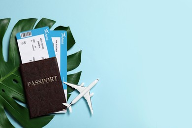Photo of Passport with tickets, airplane model and tropical leaf on light blue background, flat lay. Space for text