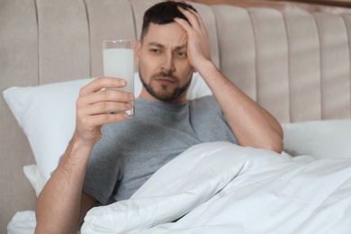 Man taking medicine for hangover in bed at home, focus on hand with glass