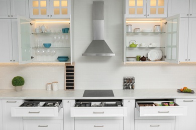 Open cabinets with different clean tableware and utensils in kitchen