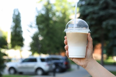 Woman holding plastic takeaway cup of delicious iced coffee outdoors, closeup. Space for text