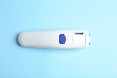 Modern non-contact infrared thermometer on light blue background, top view