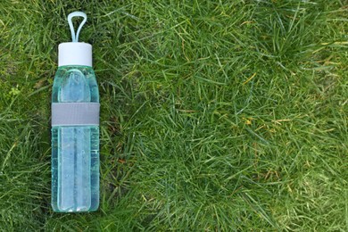 Photo of Glass bottle of fresh water on green grass outdoors, top view. Space for text