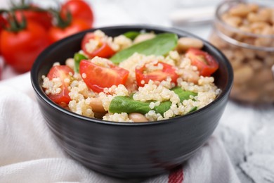 Photo of Delicious quinoa salad with tomatoes, beans and spinach leaves served on white table