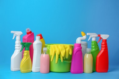 Photo of Green bucket, gloves and bottles of detergents on light blue background. Cleaning supplies