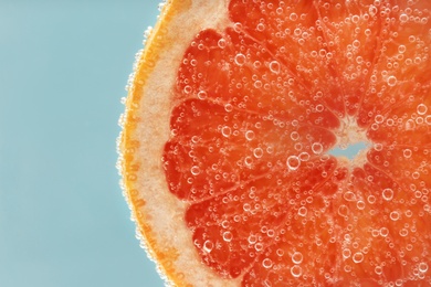 Slice of grapefruit in sparkling water on light blue background, closeup. Citrus soda