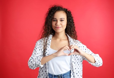 Happy young African-American woman making heart with hands on red background