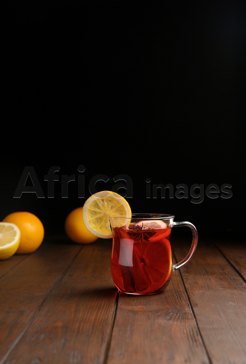 Cup with red mulled wine on wooden table against dark background. Space for text