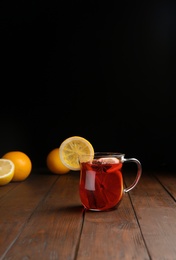 Cup with red mulled wine on wooden table against dark background. Space for text
