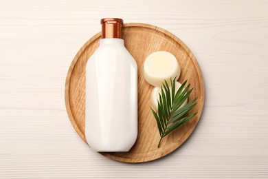 Photo of Shampoo bottle, solid shampoo bars and green leaf on white wooden table, top view