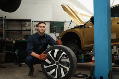Photo of Portrait of professional mechanic with car wheel at automobile repair shop