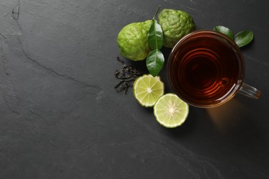 Photo of Glass cup of tasty bergamot tea, dry leaves and fresh fruits on black table, flat lay. Space for text