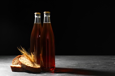Photo of Bottles of delicious fresh kvass, spikelets and bread on grey table. Space for text