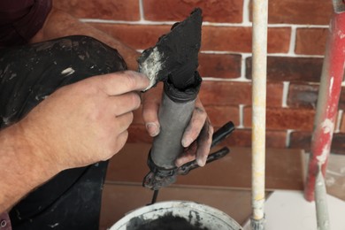 Professional builder filling fugue with grout gun near brick wall, closeup. Tiles installation process