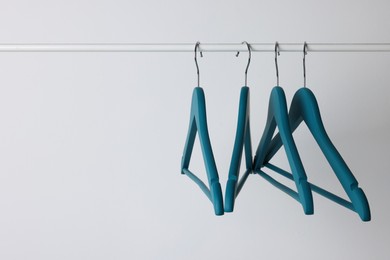 Blue clothes hangers on metal rail against light background. Space for text