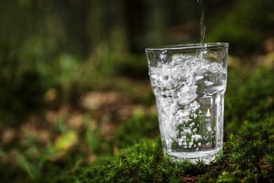 Photo of Pouring water into glass on green grass outdoors. Space for text