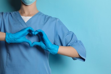 Doctor making heart with hands on light blue background, closeup. Space for text