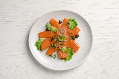 Salmon carpaccio with capers, lettuce, microgreens and onion on white wooden table, top view