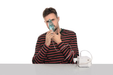 Sick man using nebulizer for inhalation at table on white background