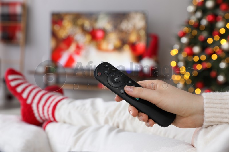 Woman with remote control watching TV at home, closeup