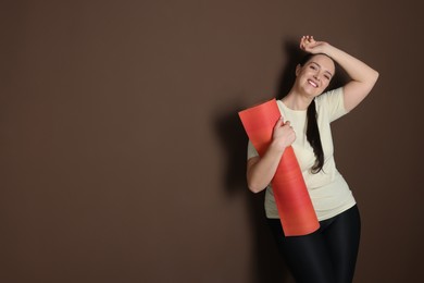Photo of Happy overweight woman with yoga mat on brown background, space for text