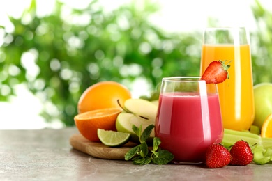 Glasses with different juices and fresh fruits on table against blurred background. Space for text