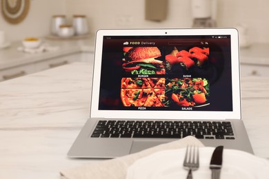 Modern laptop with open page for online food ordering on table in kitchen. Delivery service