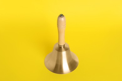 Golden school bell with wooden handle on yellow background