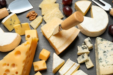 Cheese platter with specialized cutlery on black table, closeup view