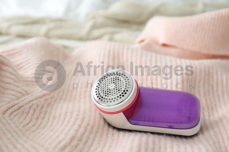 Photo of Modern fabric shaver on pink woolen sweater, closeup. Space for text