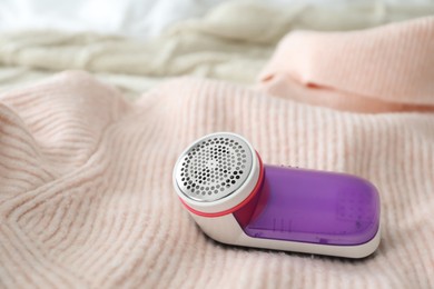 Photo of Modern fabric shaver on pink woolen sweater, closeup. Space for text