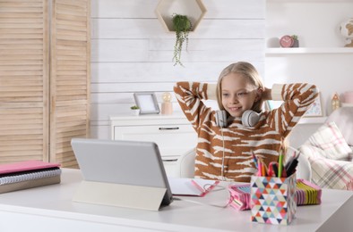 Photo of Cute little girl with modern tablet studying online at home, space for text. E-learning