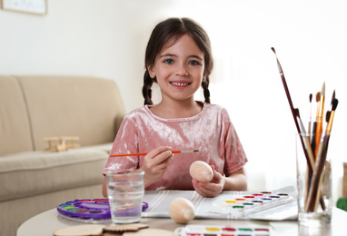 Little girl painting decorative egg at table indoors. Creative hobby