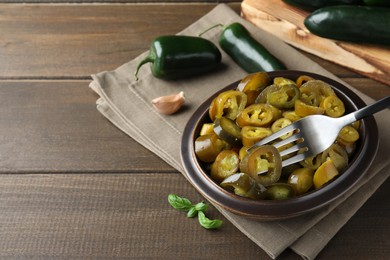 Photo of Taking slice of pickled green jalapeno with fork from bowl on wooden table, space for text