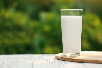 Glass of tasty fresh milk on white wooden table against blurred background, space for text