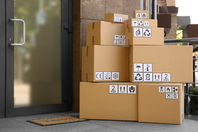 Cardboard boxes with different packaging symbols on porch near entrance. Parcel delivery