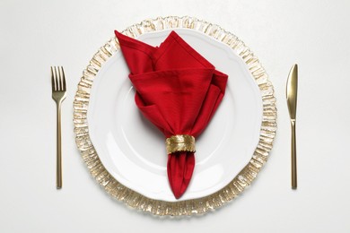 Photo of Plate with red fabric napkin, decorative ring and cutlery on white table, flat lay