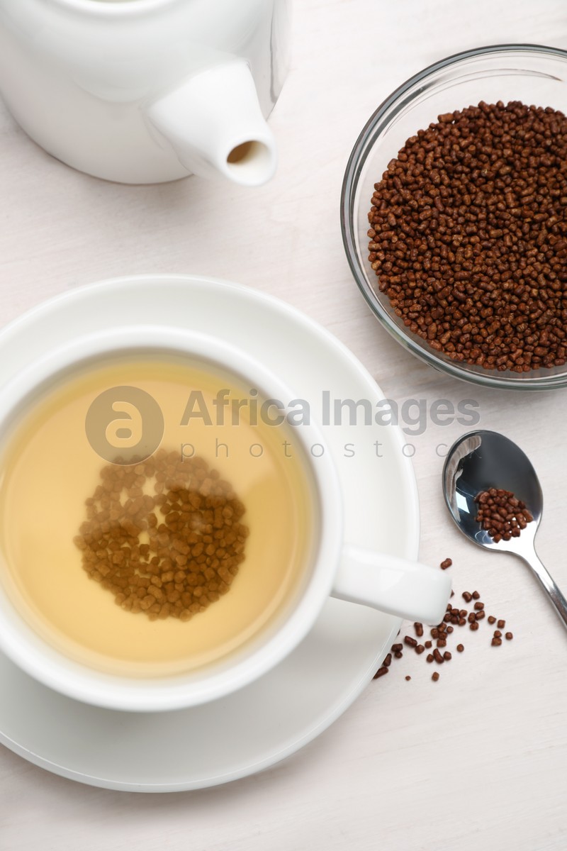 Photo of Cup of buckwheat tea, granules and teapot on white wooden table, flat lay